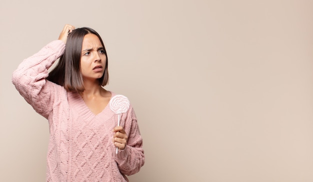 Young woman feeling puzzled and confused, scratching head and looking to the side