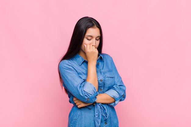 Young woman feeling serious, thoughtful and concerned, staring sideways with hand pressed against chin