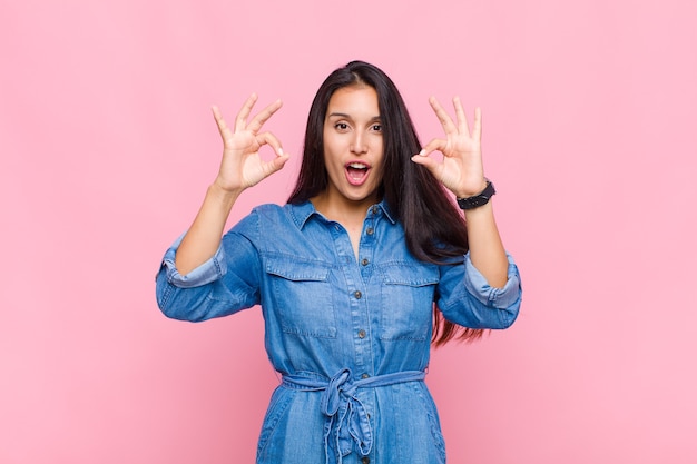 Young woman feeling shocked, amazed and surprised, showing approval making okay sign with both hands