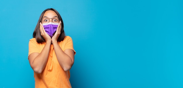 Young woman feeling shocked and scared, looking terrified with open mouth and hands on cheeks