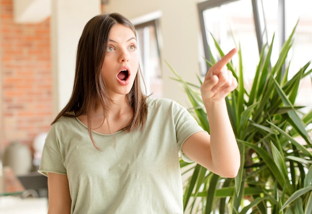 Young woman feeling shocked and surprised pointing and looking upwards in awe with amazed openmouthed look