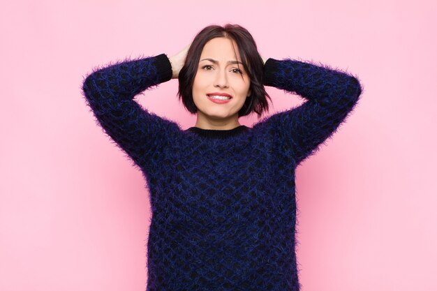 Young woman feeling stressed, worried, anxious or scared, with hands on head, panicking at mistake on pink wall