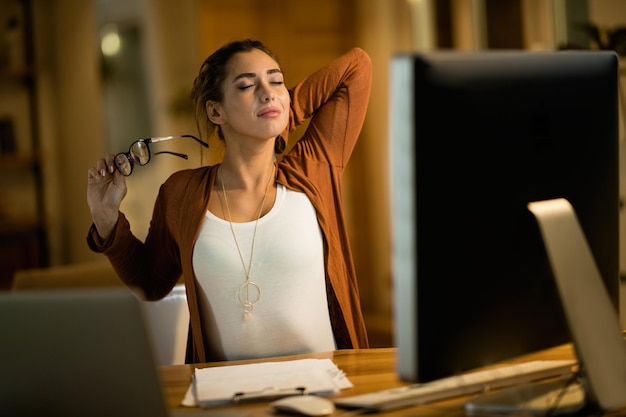 Young woman feeling tired and stretching while working late in the evening at home