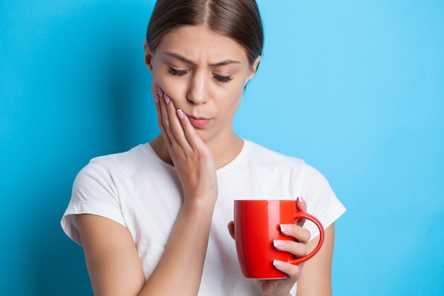 Una giovane donna sente mal di denti e tiene il posto del dolore con le mani