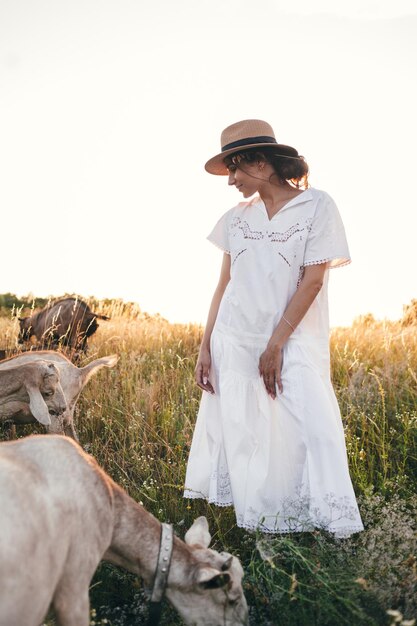 Young woman in the field is walking with goats The girl and goats in the meadow in summer Love for animals Goat farm Pets Happy woman with animal Kindness and love for animals Kisses a pet