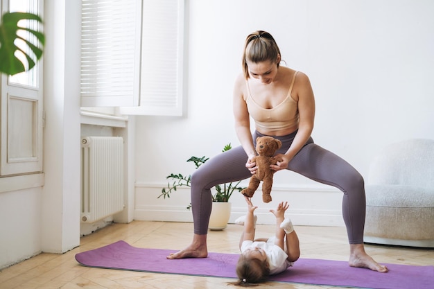 young woman fit mom with baby girl doing fitness on mat at home