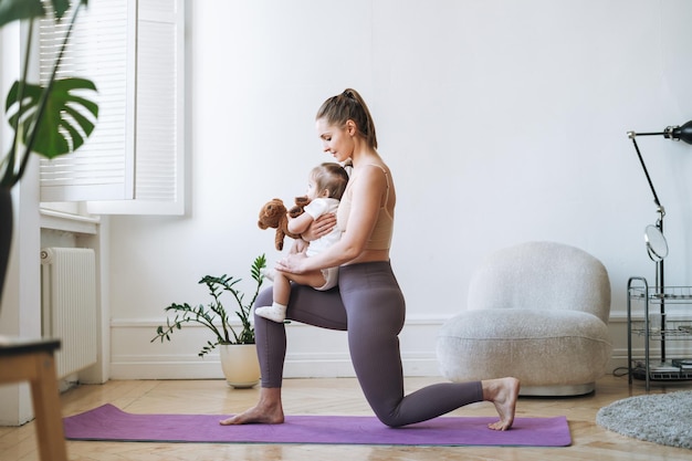 young woman fit mom with baby girl in her arms doing fitness on mat at home
