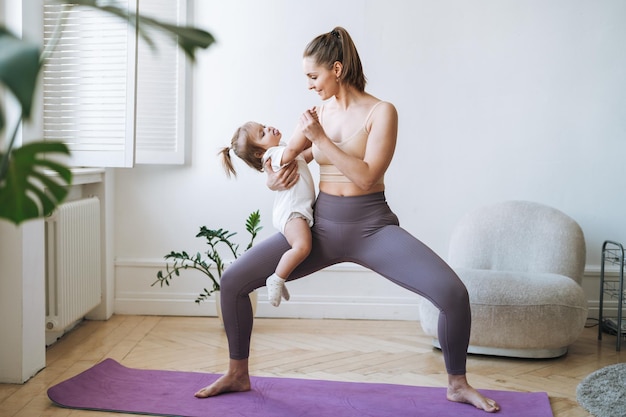 young woman fit mom with baby girl in her arms doing fitness on mat at home