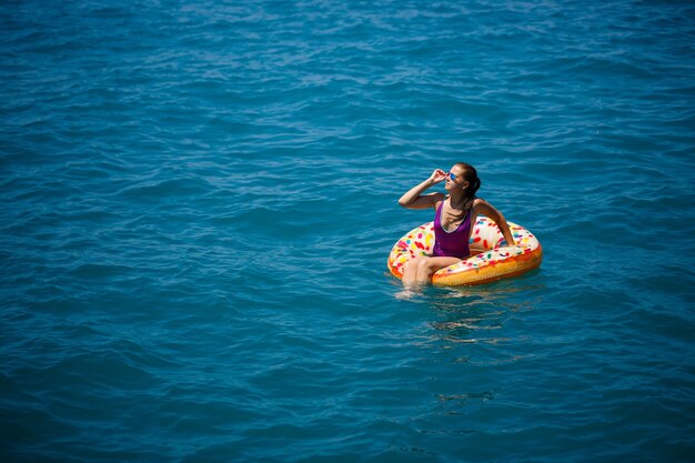 Young woman floating on an inflatable big donut in the transparent turquoise sea. View of a slender lady relaxing on vacation in Turkey, Egypt, Mediterranean Sea.