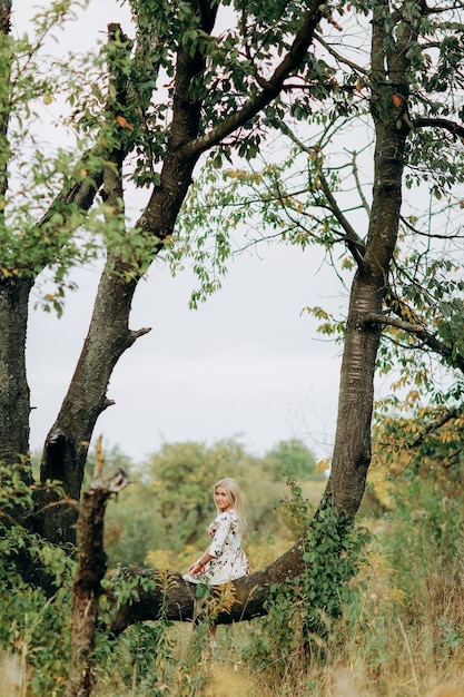 木の上に座っている花柄のドレスの若い女性
