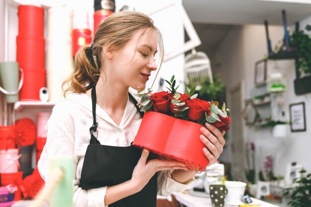 Young woman florist in black apron holds in hands hat-box with flowers
