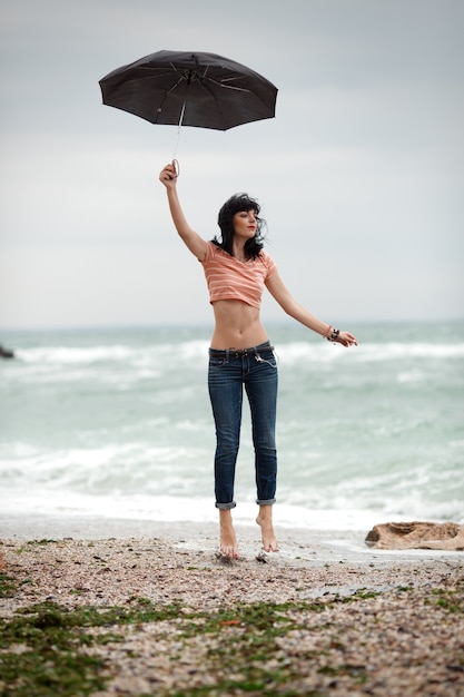 Young woman flying with umbrella near the sea. 