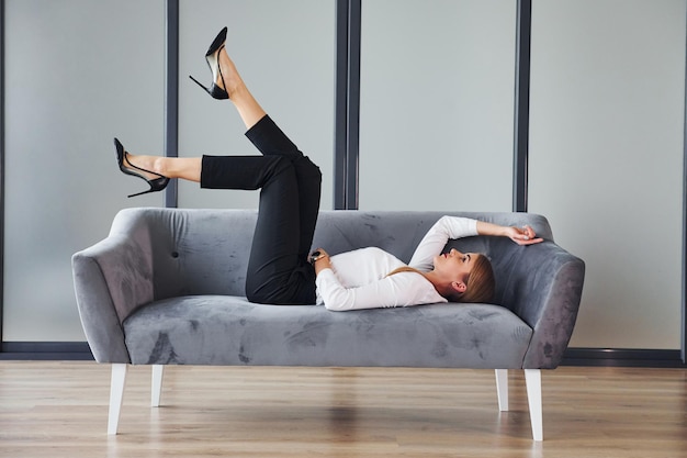 Young woman in formal clothes is indoors on the sofa at daytime