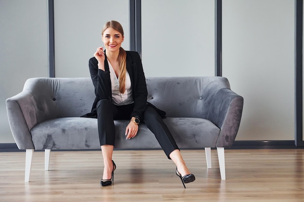 フォーマルな服を着た若い女性は、昼間はソファの上に屋内にいます