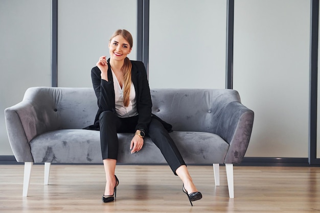 Young woman in formal clothes is indoors on the sofa at daytime