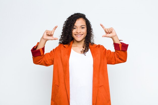 Young woman framing or outlining own smile with both hands, looking positive and happy, wellness concept over white wall