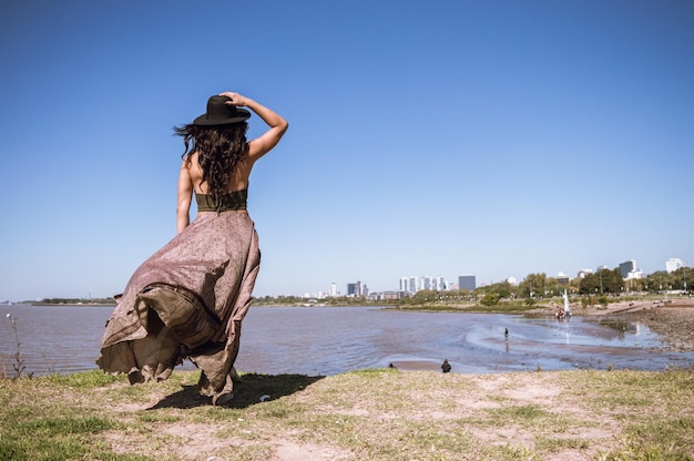 Young woman from the back with a beach dress and hat watching the coast of the city of Buenos Aires