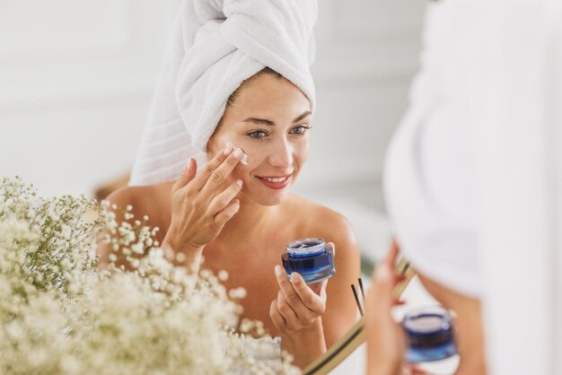 Young woman in front of mirror going through her morning beauty routine in the bathroom at home.