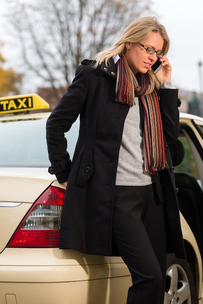 Giovane donna di fronte a un taxi con il telefono