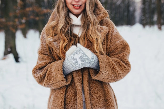 Young woman in fur coat, gloves and scarf in snowy forest. 