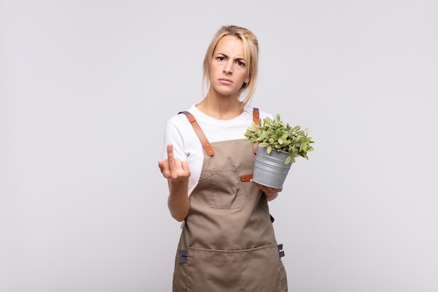 Young woman gardener feeling angry, annoyed, rebellious and aggressive, flipping the middle finger, fighting back