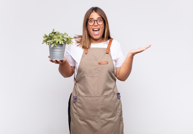 Young woman gardener feeling happy, excited, surprised or shocked, smiling and astonished at something unbelievable