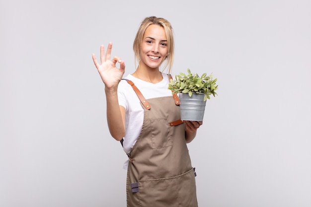 Молодая женщина-садовник чувствует себя счастливой, расслабленной и удовлетворенной, демонстрирует одобрение жестом, улыбаясь