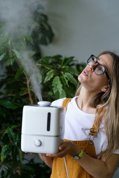 Young woman gardener hold air humidifier in indoor garden to save houseplants while heating season