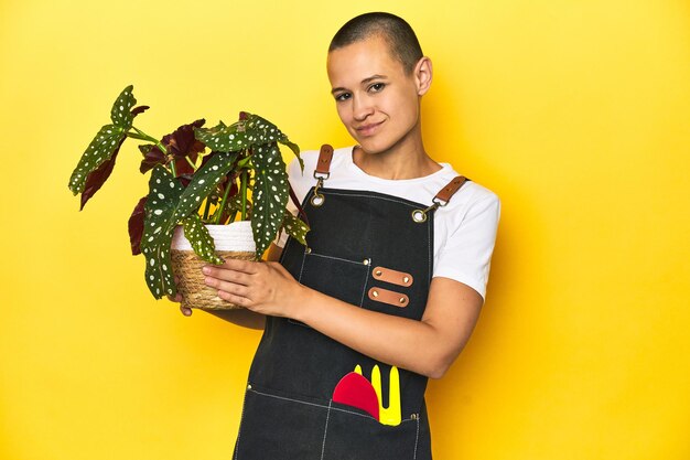 Young woman gardener holding plant yellow studio background