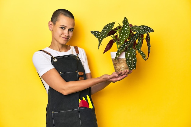 Young woman gardener holding plant yellow studio background