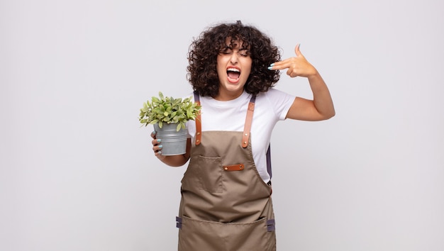 Young woman gardener looking unhappy and stressed, suicide gesture making gun sign with hand, pointing to head