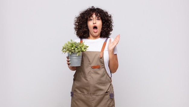 Young woman gardener looking very shocked or surprised, staring with open mouth saying wow