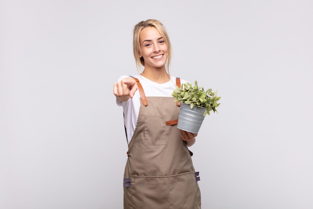 Giardiniere della giovane donna che indica alla macchina fotografica con un sorriso soddisfatto, sicuro, amichevole, scegliendo te