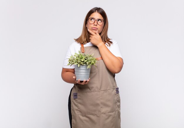 Young woman gardener thinking, feeling doubtful and confused, with different options, wondering which decision to make