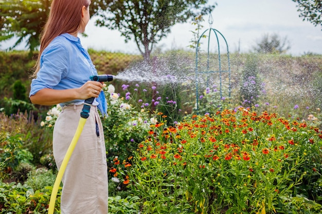 夏の庭でホースパイプで植物に水を注ぐ若い女性ガーデナー開花する花の世話屋外活動