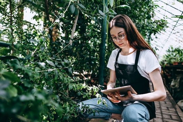 Young woman gardener with digital tablet working in greenhouse