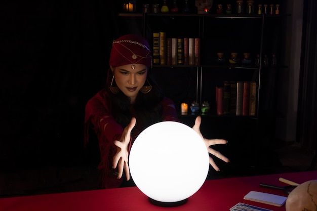 Foto giovane donna che gesticola sulla palla di cristallo mentre è seduta nella camera oscura