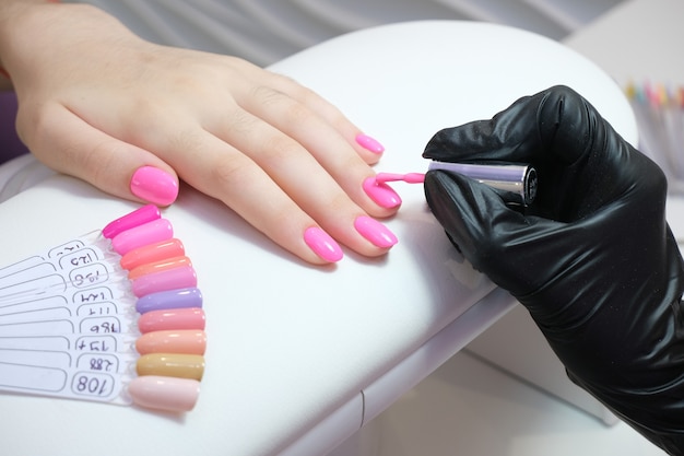 Young woman gets a manicure in the salon. applying shellac to the nails. pink color