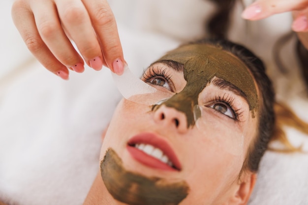 Young woman getting eye patches and face treatment with seaweed mud at the spa.