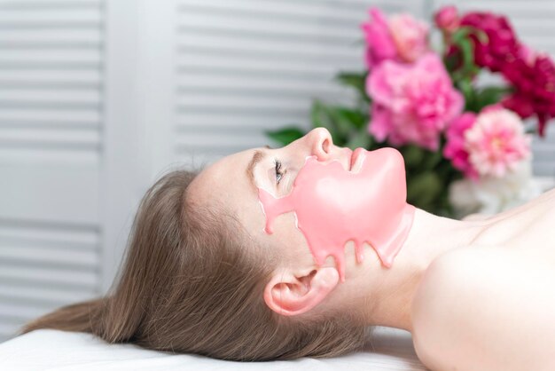 Young woman getting facial skin cosmetic procedure in beauty salon Alginate face mask Close up