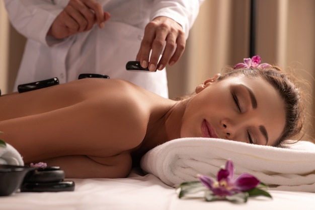 Young woman getting hot stone massage in spa salon. Beauty treatment concept.