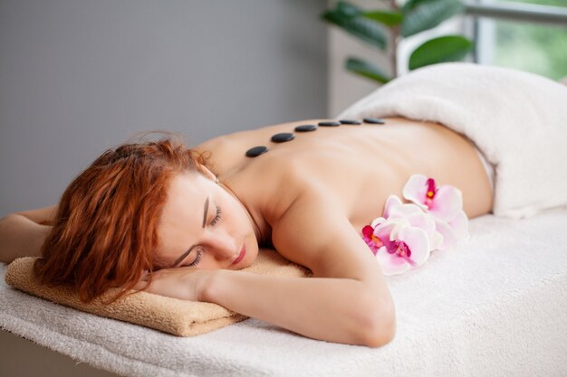 Young woman getting hot stone massage in spa salon.