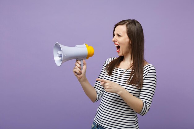 Young woman girl in casual striped clothes posing isolated on
violet background studio portrait. people lifestyle concept. mock
up copy space. scream in megaphone, announces discounts sale hurry
up.