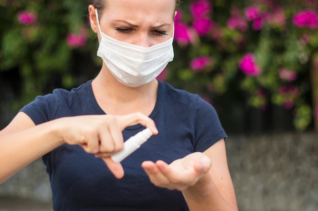 Young woman girl disinfects hands, girl in protective sterile medical mask on face