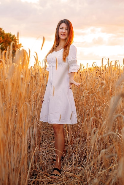 a young woman or girl in a field with wheat walks at sunset