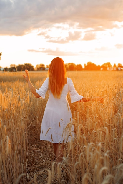 a young woman or girl in a field with wheat walks at sunset