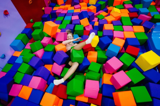 A young woman or girl, mother playing and jumping in soft cubes in the dry pool of the game children's room for birthday. entertainment centre. indoor playground in foam rubber pit in trampoline.