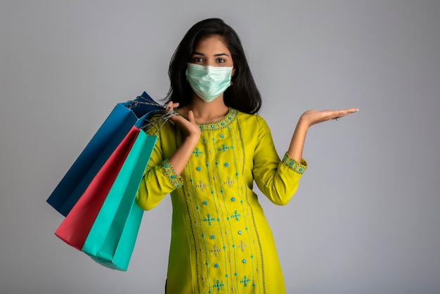 Young woman girl wearing medical mask holding shopping bags on grey background. Shopping discount sale concept.