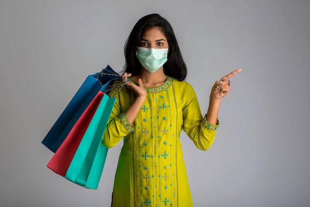 Young woman girl wearing medical mask holding shopping bags on grey background. shopping discount sale concept.