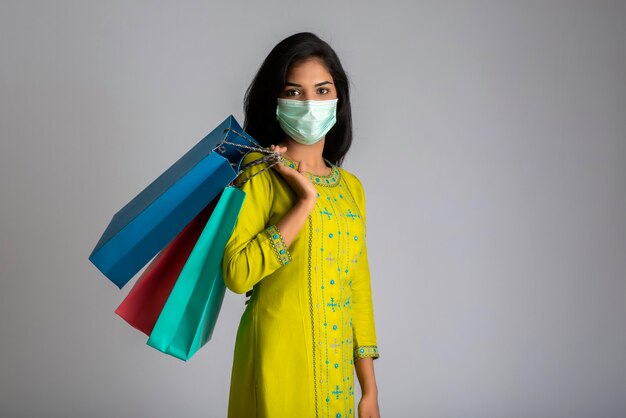 Young woman girl wearing medical mask holding shopping bags on grey background. Shopping discount sale concept.